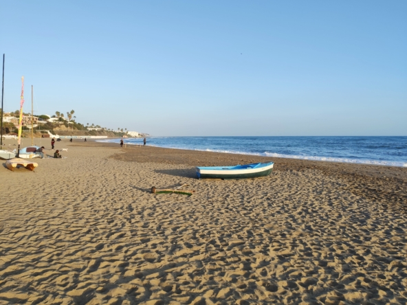 Sunset view of La Cala de Mijas beach with palm trees and ocean waves.