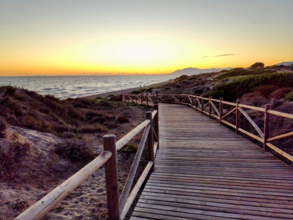 Sunset at Costa del Sol, with a wooden boardwalk leading through dunes to the beach, reflecting the area's serene beauty and inviting exploration
